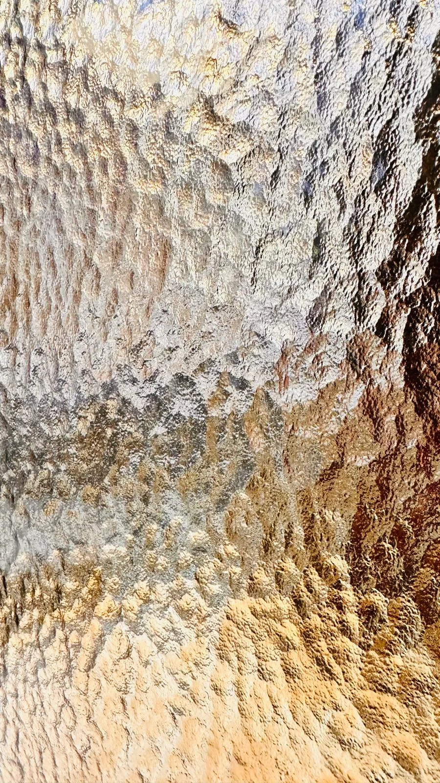 Close-up of a softly hammered glass surface reflecting silver and warm gold